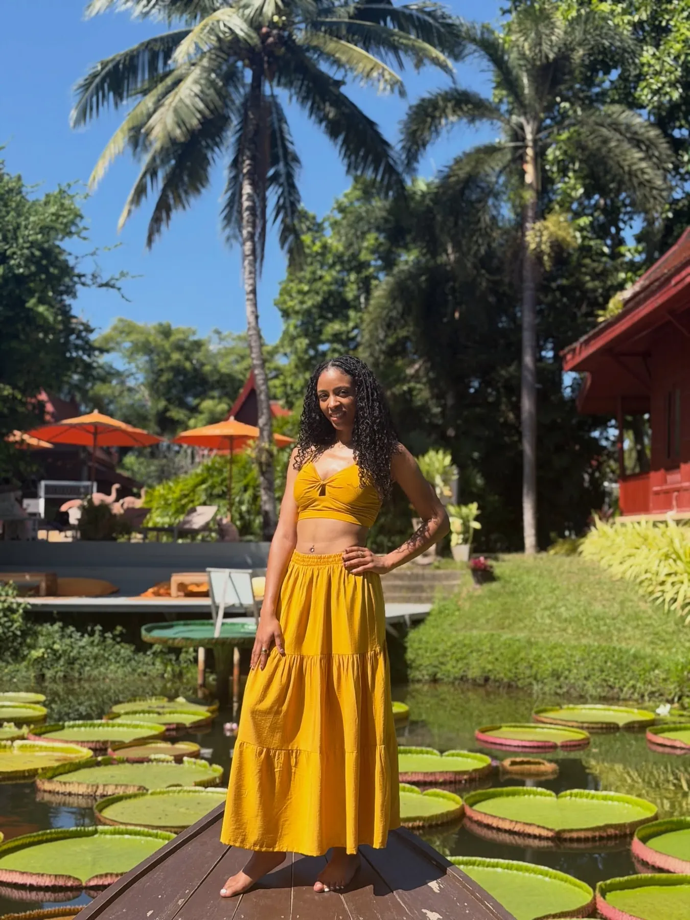 Kay in a yellow outfit standing on a wooden boat among giant lily pads in Thailand